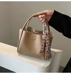 Detail of beige lychee texture bucket bag featuring a decorative brown plaid silk scarf handle