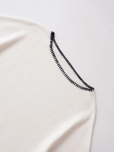Detail of white knit vest with black blanket stitch trim showing fabric texture
