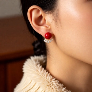 Detail view of a vintage pearl earring with a large red bead and gold leaf design