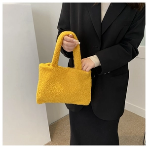 Detail of yellow teddy plush tote bag held by model wearing a black blazer