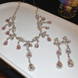 Detailed view of silver jewelry set with pink teardrop crystals on white tray