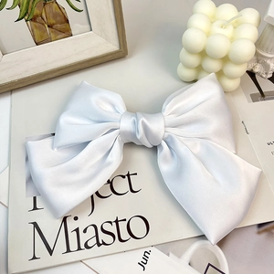 Detailed view of a white satin oversized bow hair clip on a minimalist aesthetic magazine