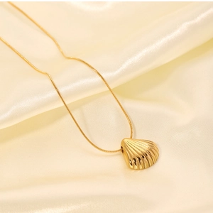 Close-up of gold shell pendant on snake chain over champagne satin fabric