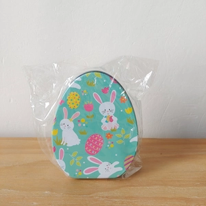 Detailed view of an egg-shaped Easter tin box with rabbit pattern in clear polybag