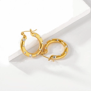 Detail of gold-plated hoop earrings featuring inlaid clear crystals on a white stone base