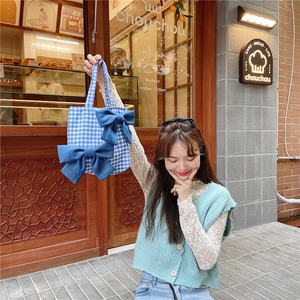 Close-up of a blue and white gingham tote bag with two denim bows in a street setting