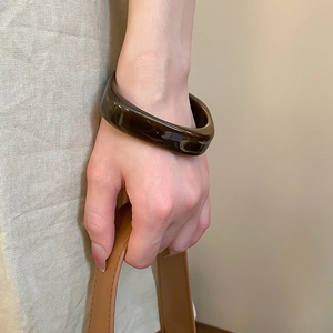 Nahaufnahme eines wellenförmigen Bernstein-Resin-Armreifs am Handgelenk in Erdtönen
