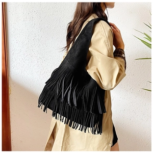 Side view of black faux suede hobo bag with tiered fringes worn by a model in a studio