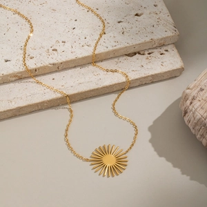 Détail d'un collier avec pendentif soleil doré sur un fond en pierre naturelle