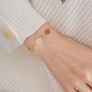 Close-up of a gold clover hollow charm bracelet worn over a white sweater cuff