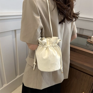 Chic white drawstring bucket bag shown from a side view on model in a soft beige suit