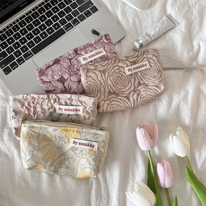 French embossed floral makeup bags in assorted colors and patterns on a soft bed