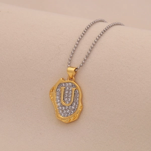 Macro shot of gold-tone pendant with clear crystals and letter U on silver ball chain