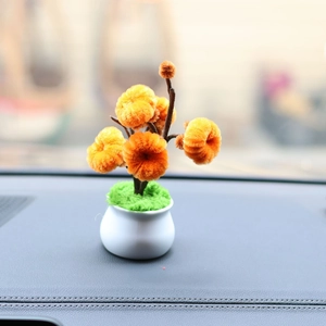 Close-up of handmade orange plush sunflower plant in white pot on car dashboard