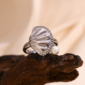 Macro shot of silver scallop shell ring with embedded diamonds and a white pearl on wood