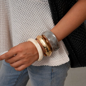Bracciali impilabili in resina marmorizzata e metallo dorato lucido su un polso