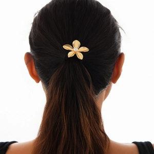 Close-up of golden flower hair tie with pearl center worn on long dark hair