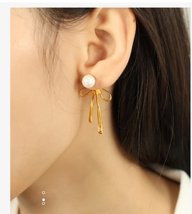 Close-up of model wearing gold bow earrings with elegant white pearls for women