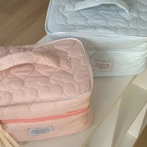 Detailed view of pink and blue quilted heart makeup bags with zipper on white shelf