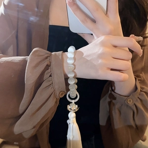 Close-up of cat-eye stone lotus bracelet with white silk tassel detail on wrist