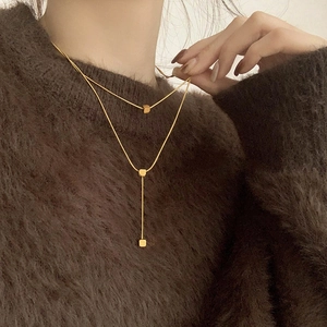 Detail shot of golden double-layer necklace with geometric cube pendants on a model