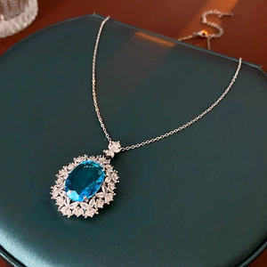 Detailed view of an oval blue zircon necklace with floral accents on a velvet box