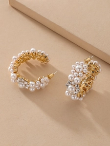 Detail of C-shaped gold earrings with clustered white pearls and rhinestone flowers