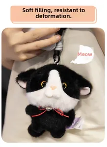 Close-up of black and white plush cat keychain with red ribbon and silver bell detail