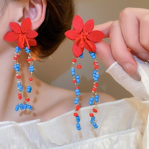 Dettaglio di orecchini a fiore rossi con lunghe nappe di perline su modella