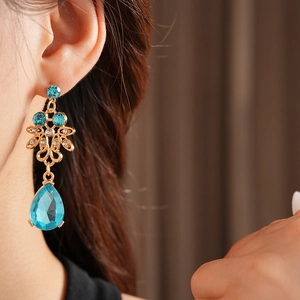 Close-up of vintage gold drop earrings with blue gemstones and diamonds on a model