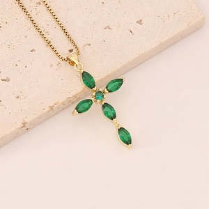 Gold cross necklace featuring marquise-cut green zircon stones on a beige stone background