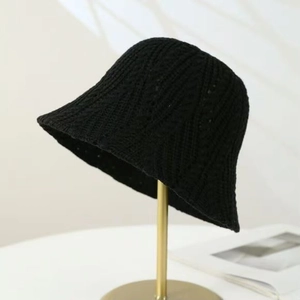 Close-up of black knitted bucket hat with hollow texture on a gold metal stand