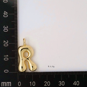 Macro shot of golden letter R balloon pendant with measurement ruler and weight info