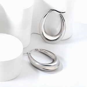 Polished silver stainless steel chunky oval hoop earrings on geometric display stand
