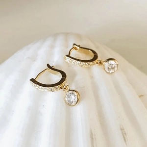Elegant gold hoop earrings with sparkling zircon drop pendants on a white shell background