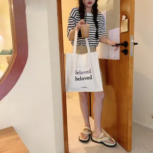 Détail du sac cabas en toile blanc cassé avec broderie beloved dans un café moderne