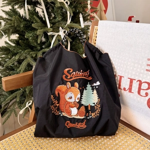 Detail of embroidered squirrel on black nylon tote bag with festive Christmas tree background