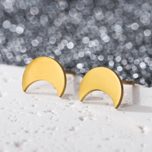 Close-up of golden crescent moon studs on textured white stone with bokeh background