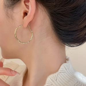 Detail view of gold twisted hoop earrings worn by a model in a minimalist style