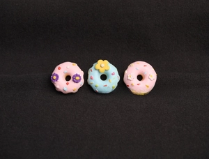 Detailed view of three resin donut pins with colorful flower patterns on a dark surface