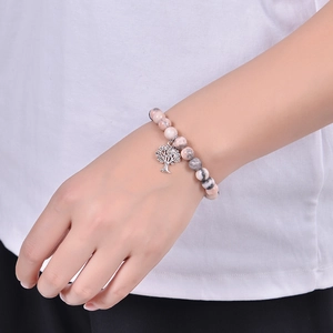 Close-up of pink zebra stone beaded bracelet with tree of life charm worn by a model