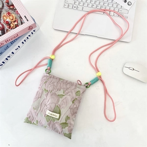 Floral jacquard crossbody bag in pink and green with woven strap on a white desk setup