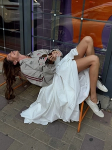 Street style shot of a white tiered maxi skirt paired with a taupe racing jacket
