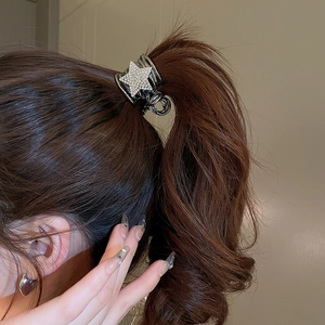 Detailed view of a sparkling rhinestone star hair claw clip on a brown wavy ponytail