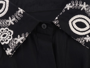 Detail of white floral embroidery on a black button-up shirt collar and fabric texture
