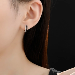 Close-up of model wearing geometric silver hoop earrings with black enamel and zircon