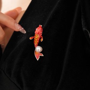 Detail of red enamel koi fish brooch with golden base and pearl on black velvet