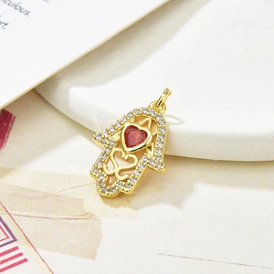 Macro shot of gold Hamsa hand pendant with red heart gemstone and clear zircon accents