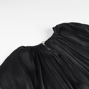 Close-up of black pleated fabric neckline featuring a delicate pearl button detail