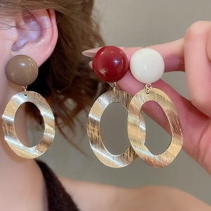 Detail of brushed gold oval earrings with colorful resin studs in red and brown
